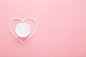 White heart shapes with cream jar on light pink table background. Pastel color. Care about female face, hands, legs and body skin. Closeup. Empty place for text. Top down view. - 790103195