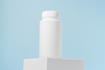 White pill jar mockup on a pedestal on a blue background. Concept of pharmacy, medicine, health care and dietary supplements.