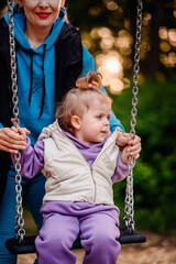 A mother gently supports her little one on a swing, with the toddler's expression of curiosity capturing the simple joys of a new experience