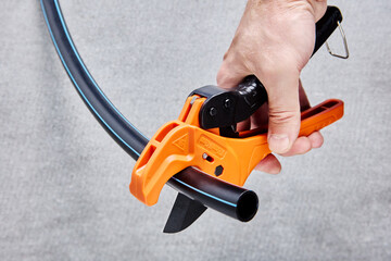 Ratchet pipe cutter is cutting flexible HDPE tube.