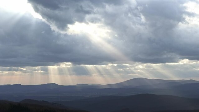 timelapse of storm clouds through which rays of light shine on the landscape below