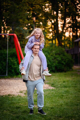 In the soft light of sunset, an adult gives a piggyback ride to a delighted child in a park, with...