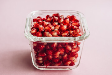 Viele frische, rote, saftige Kerne von Granatapfel, Granatapfelkerne in einem Glas auf rosa Hintergrund