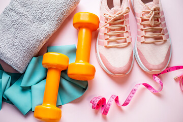 Fitness concept. Sneakers, dumbbells, towel and measuring tape on pink background top view