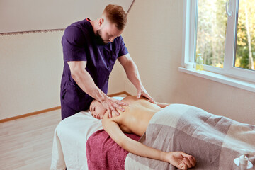 Massage therapist services at home, masseur kneads back muscles of young woman in her home.