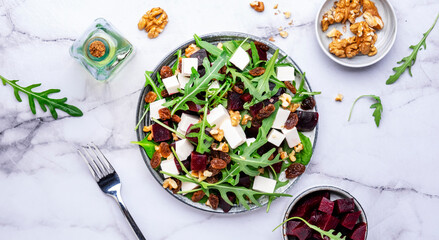 Beetroot and white cheese salad with arugula, lettuce, chard and walnuts, white table, copy space. Fresh useful vegetarian dish for healthy eating