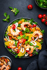 Delicious salad with shrimp, mussels, squid, oranges, lamb lettuce and olive oil with lemon juice dressing, black table background, top view - 790155911