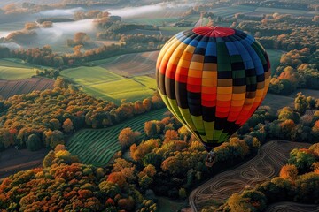 Obraz premium A colorful hot air balloon drifting gracefully over a patchwork landscape of fields and forests.
