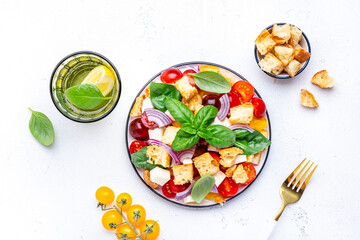 Fresh summer salad with tomatoes, stale bread, onion, cheese, green basil and olive oil, white table background, top view
