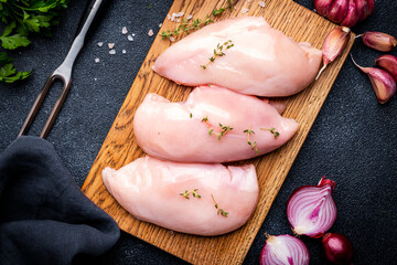 Raw chicken breast fillet on wooden cutting board, black table background, top view