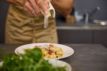 Close-up chef's hands seasoning and decorating meal with parmesan cheese and fresh arugula leaves, cooking pasta with tomato sauce according to traditional Italian recipe. Cuisine. Culinary. Epicure