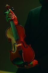 Mysterious man in black suit playing violin in front of vibrant green and red background, close up portrait © SHOTPRIME STUDIO