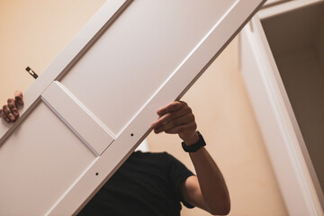 A young man holds the side door of a wardrobe.