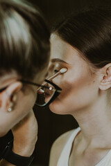 A young makeup artist applies shadows to a girl s eyelids with a brush.