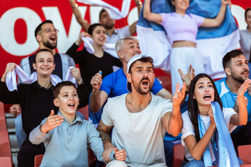 Sport fans cheering at the game on stadium. Wearing blue and white colors to support their team....