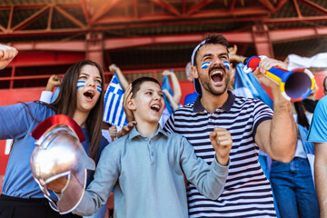 Greece fans cheering at the game on stadium. Wearing blue and white colors to support their team. Celebrating with flags and scarfs. - 790182312