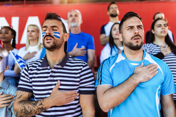 Sport fans singing national anthem of their country at the stadium. Wearing blue and white to support their team. - 790182382