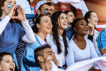 Sport fans cheering at the game on stadium. Wearing blue and white colors to support their team. Celebrating with flags and scarfs. - 790182560