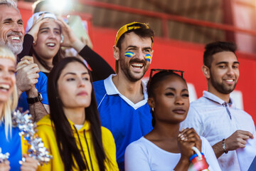 Sport fans cheering at the game on stadium. Wearing yellow and blue colors to support their team. Celebrating with flags and scarfs. - 790182716