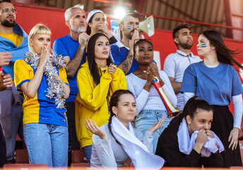 Sport fans cheering at the game on stadium. Wearing yellow and blue colors to support their team. Celebrating with flags and scarfs.