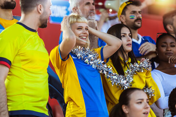 Sport fans cheering at the game on stadium. Wearing yellow and blue colors to support their team. Celebrating with flags and scarfs. - 790182789
