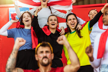 Sport fans cheering at the game on stadium. Wearing red, white and yellow colors to support their team. Celebrating with flags and scarfs. - 790182958