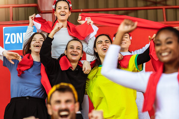 Sport fans cheering at the game on stadium. Wearing red, white and yellow colors to support their...
