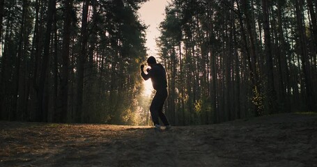 Wide shot of young man athlete training in the forest. Shadow boxing and running on sunrise in nature - Powered by Adobe