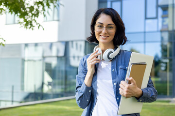Confident young student with headphones outside university