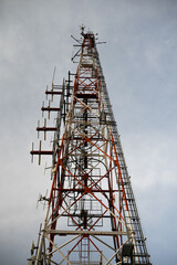Vertical metallic telecommunication tower with radio antennas with gray clouds