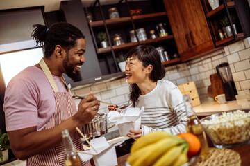 Multiracial couple eating sushi together at home.
