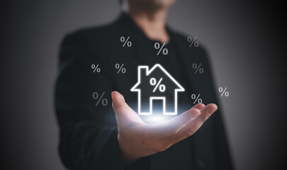 A person in a suit holds a glowing house icon with percentage symbols, symbolizing mortgage rates or real estate investment.
