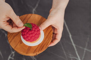 Top view of the pastry chef's hands decorating an apple-shaped cake with a green leaf.