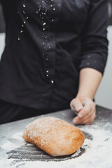 An experienced chef cooks in a professional kitchen prepares dough with flour for making ciabatta...