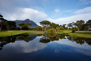 Obraz premium Grass, lake and trees on golf course with mountain, clouds and natural landscape with river in park. Nature, green and field with sustainable environment, sunshine and blue sky reflection in Canada