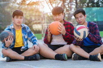 Asian boys in plaid shirt holding and waiting for basketball playing with friends at outdoor basketball court of his school,concept for freestyle and lifestyle of young teens around the world.