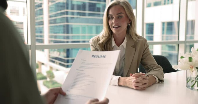 Unknown male HR manager holds in hands resume paper while interviewing young 30s confident applicant woman in modern office board room. Hiring process, human resources, headhunting, company staffing