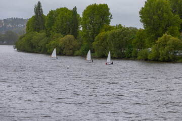 Three single-place sailboats race down a river in bad weather. The boats follow each other closely in this competition