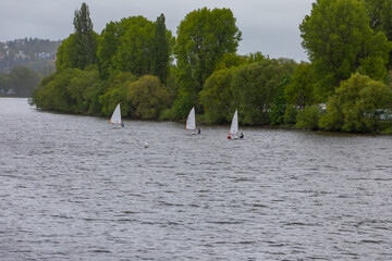 Three single-place sailboats race down a river in bad weather. The boats follow each other closely in this competition