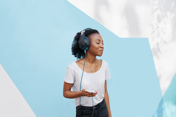Black girl, headphones and phone for music in studio, website and online for playlist on backdrop. Female person, mockup space and internet for social media, kpop and app for audio and streaming fun