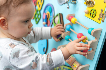 Close-up of a cute kid moving with concentration round colored wooden elements on a busy board