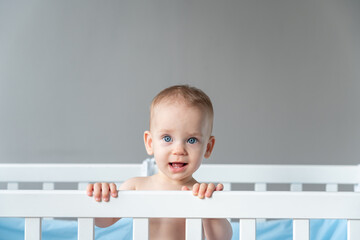 A modestly smiling baby leaned on the back of a wooden crib