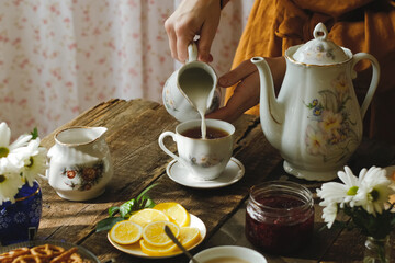Tea party in rustic style. Pouring milk into tea cup.
