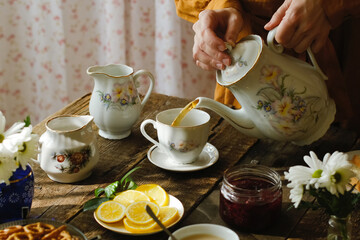 Tea party in rustic style. Pouring tea from teapot into porcelain cup.