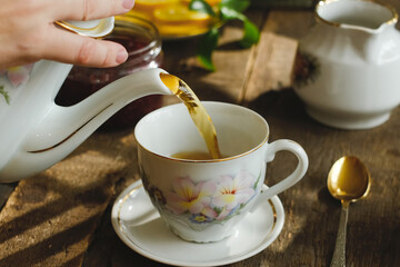 Pouring tea from teapot into porcelain cup. Morning breakfast.