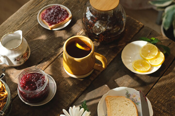 Morning breakfast. Tea cup with lemon slice and sweet food on wooden table