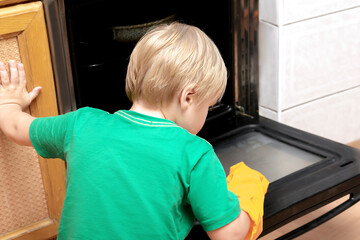 Cleaning dirty oven from grease,food leftovers deposits.Boy child in protective glove,sponge rag washing kitchen stove,helping with housekeeping, housework, home chores