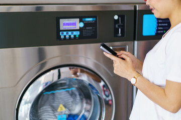 Woman using a self-service washing machine at laundry store. - obrazy, fototapety, plakaty
