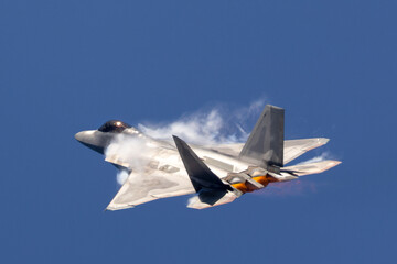 Side view of a F-22 Raptor in a high G maneuver, with afterburners on and condensation clouds at...