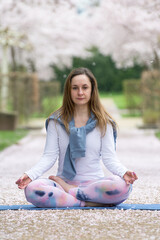 A young woman does yoga in nature in the lotus position against the backdrop of a spring blossoming sakura alley. Concept of mental and physical health and balance in life. Vertical format.